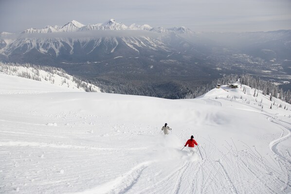 Un paysage de montagne enneigé avec deux skieurs dévalant une pente.