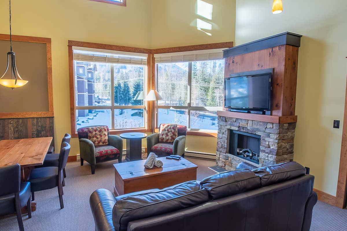 A cozy indoor seating area with a wooden table, cushioned chairs, a sofa, and a fireplace.