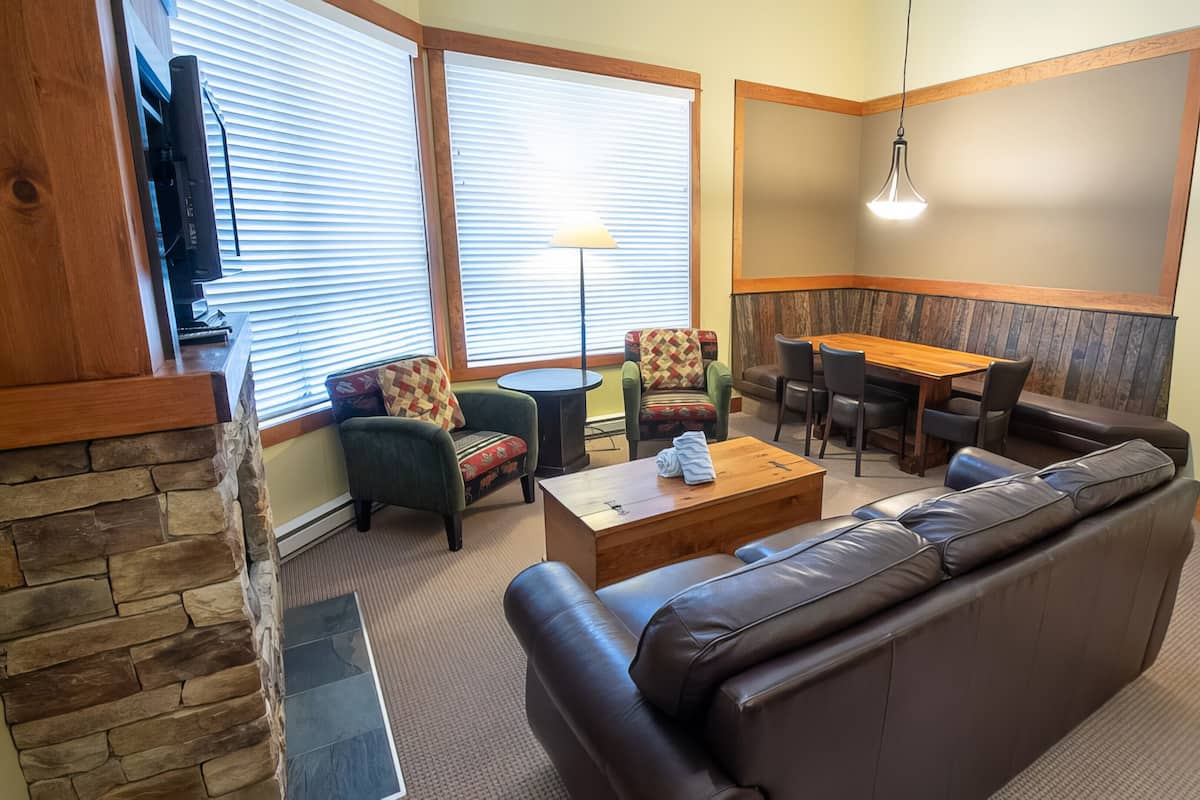 A cozy living room with a stone accent wall, a leather sofa, a wooden coffee table, and a dining area with a table and chairs.