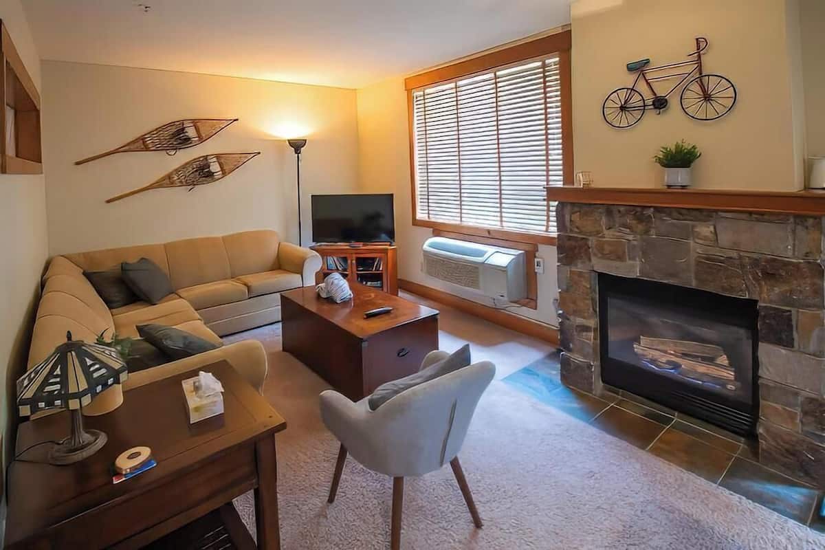 A living room with a sofa, coffee table, and armchair, a fireplace, a television, and decorative wall art.