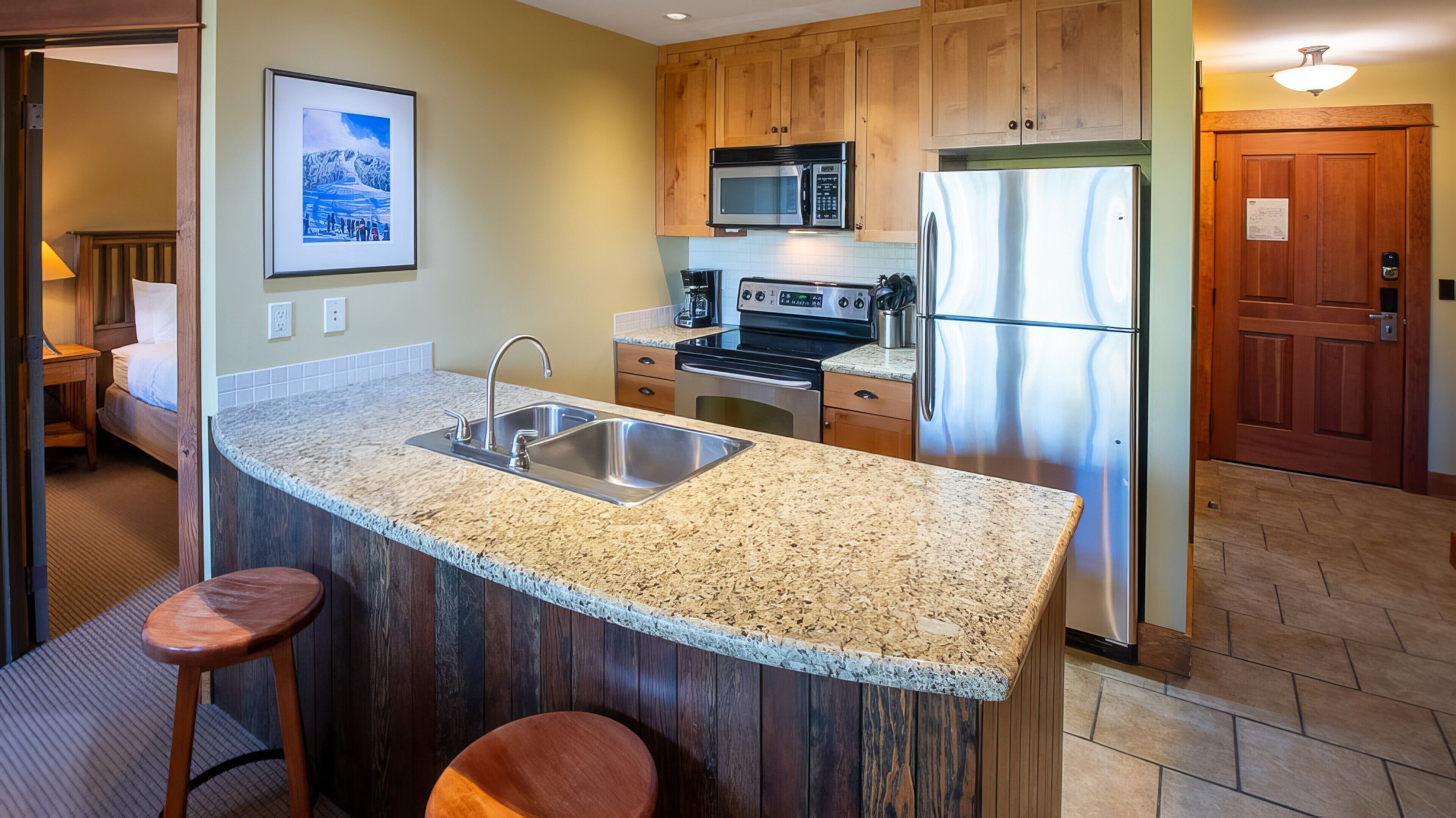 Una cocina con encimeras de granito, electrodomésticos de acero inoxidable, armarios de madera y una isla integrada con taburetes de bar.