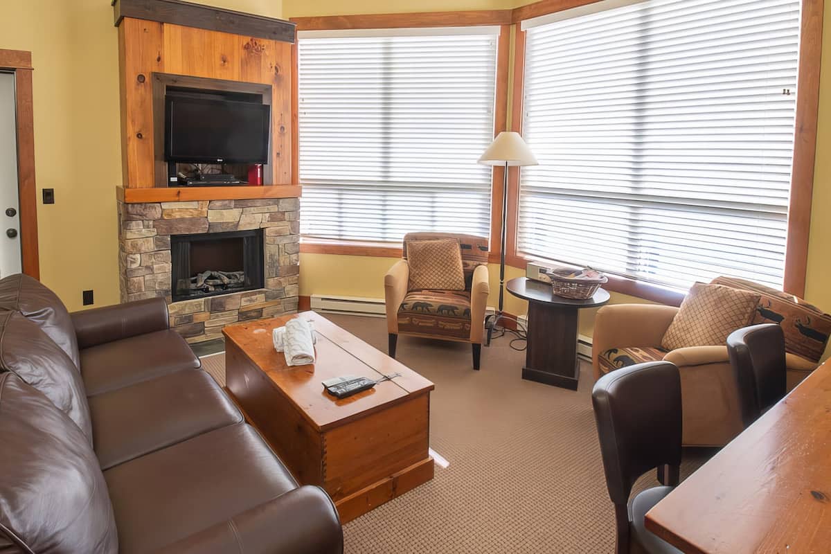 A living room with a stone fireplace, leather sofa, and a television mounted above it.