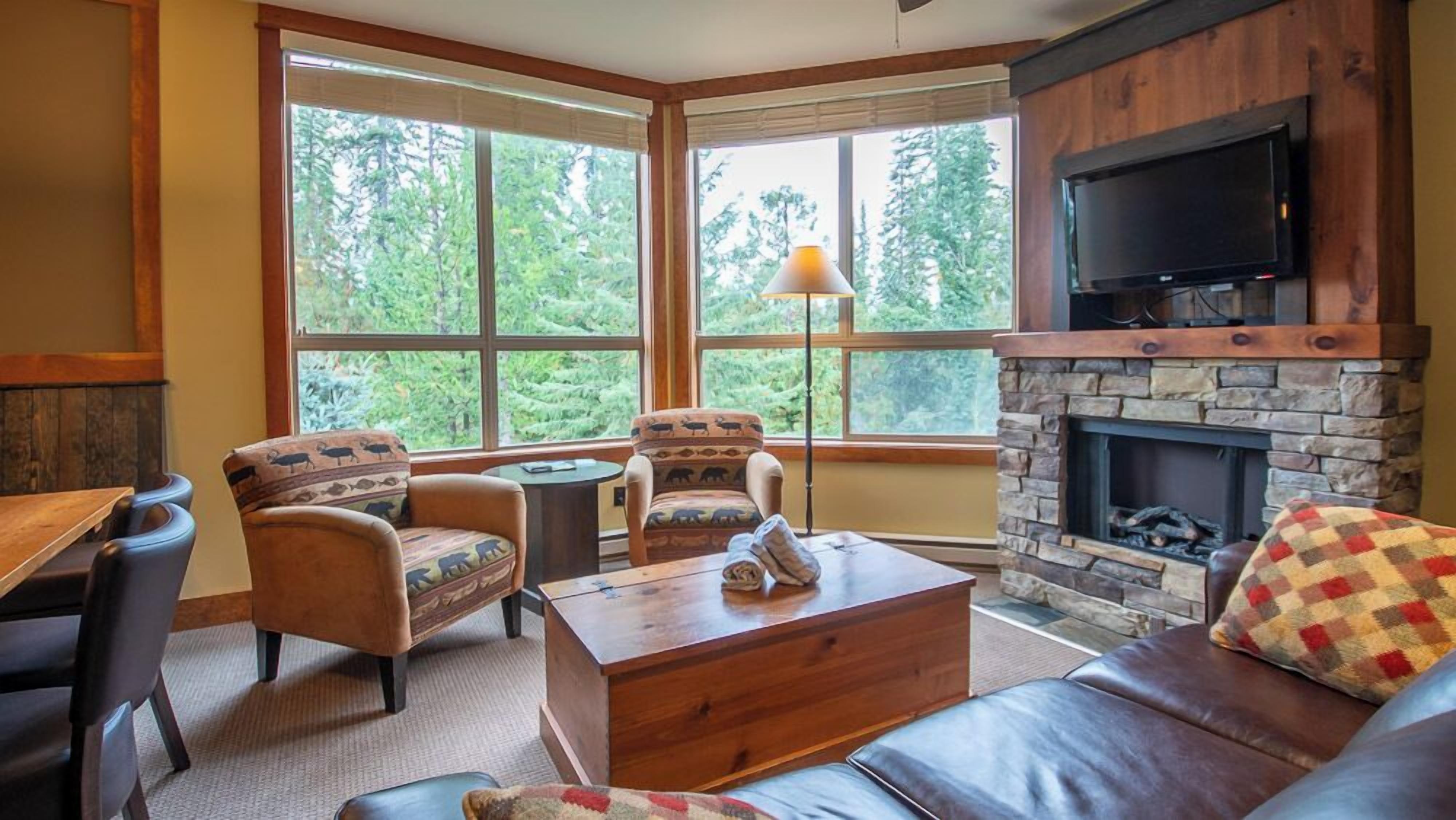 A cozy living room with a stone fireplace, large windows, and comfortable seating.
