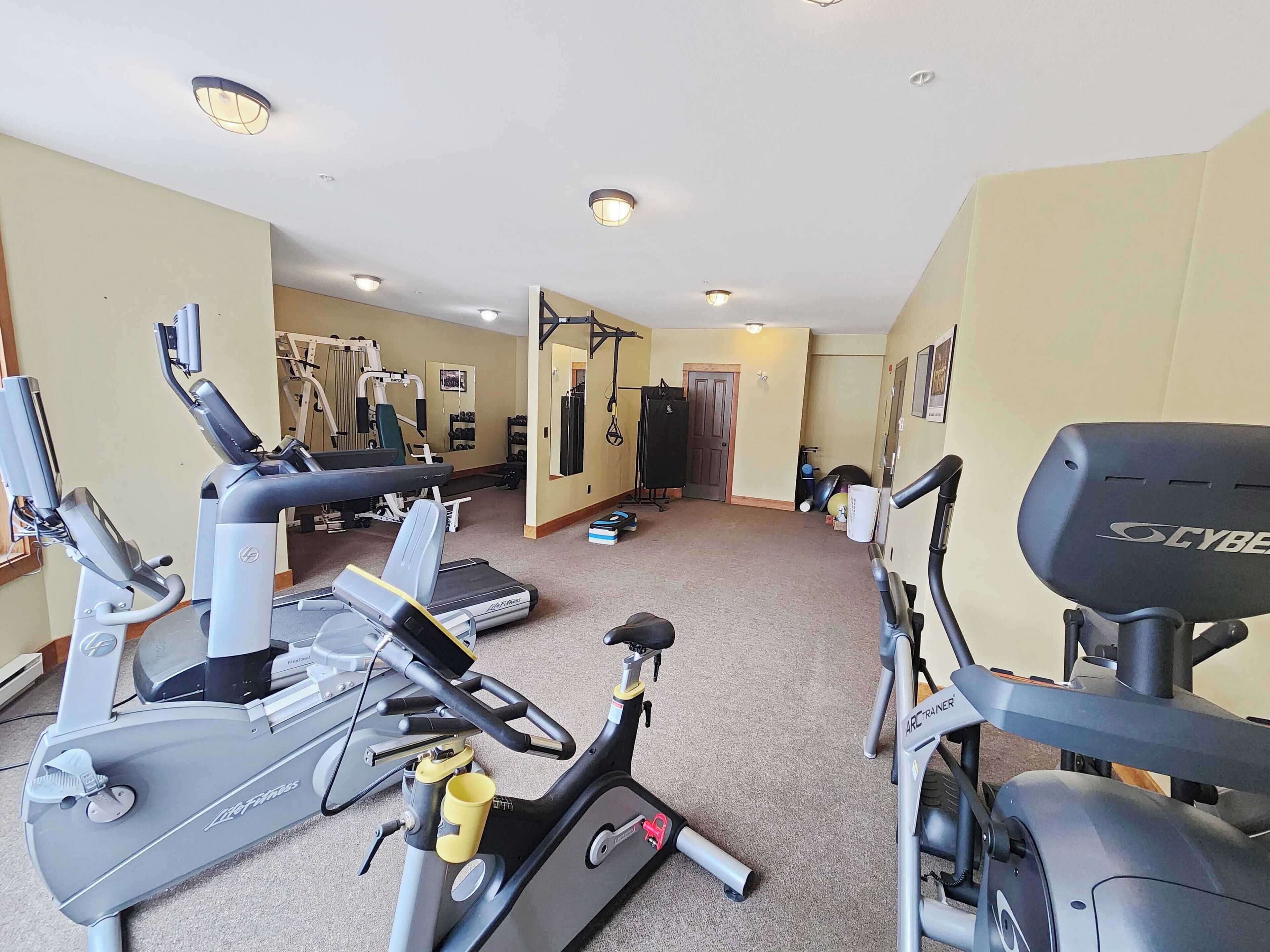 Ett gym med konditionsmaskiner, styrketräningsutrustning och en vägg full med speglar.