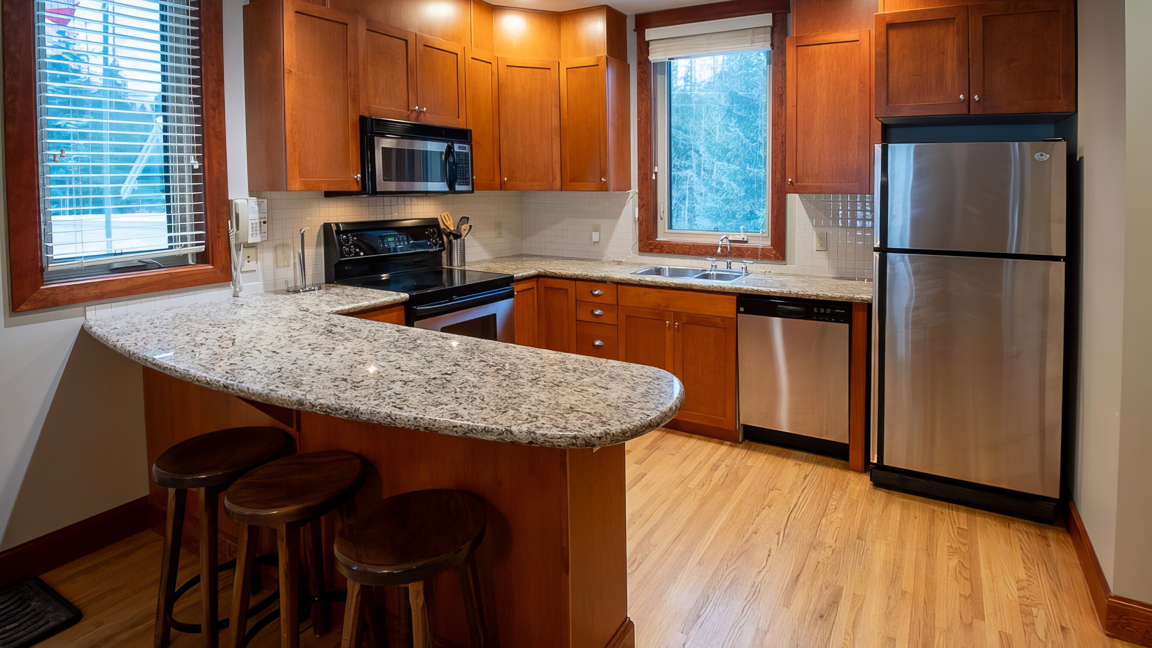 A kitchen with wooden cabinets, a stainless steel refrigerator, a built-in oven, and a granite countertop.