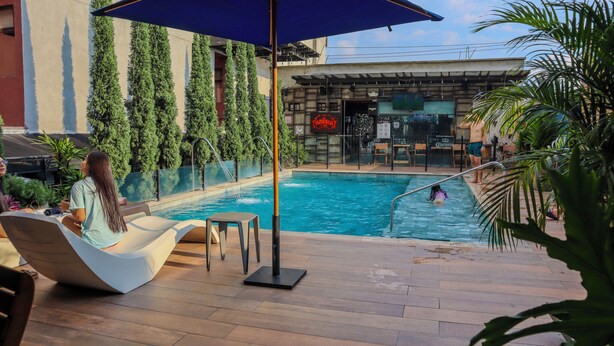 Zona de piscina con sillones de descanso, bar junto a la piscina y un letrero de Corona.