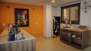 Una cocina con cafetera, refrigerador y comedor con mesa y sillas de madera.