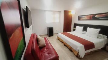 A hotel room with a bed, a red leather sofa, a TV, a window, and a wall-mounted artwork.