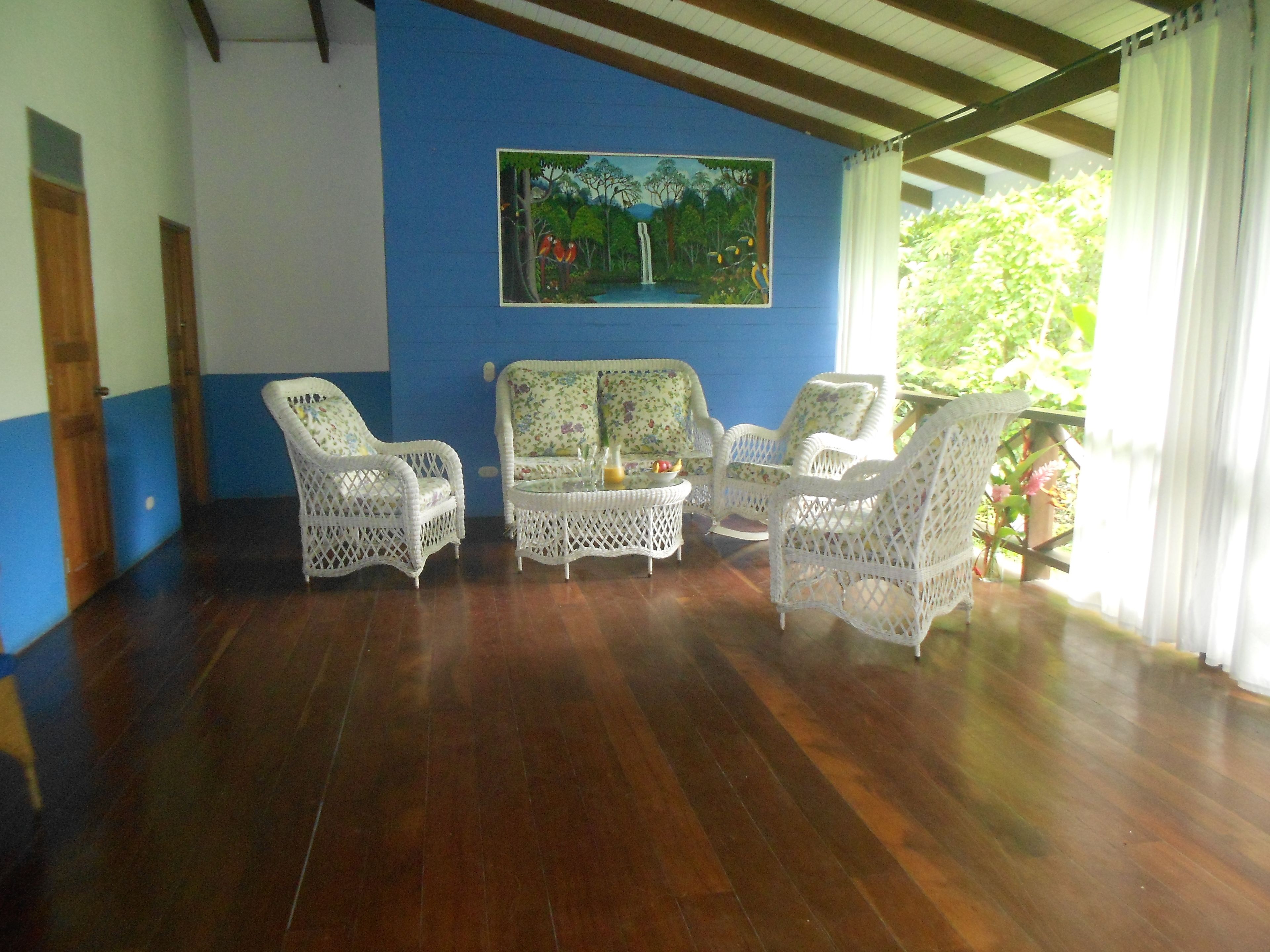 A room with a blue wall, wooden flooring, and white wicker furniture.