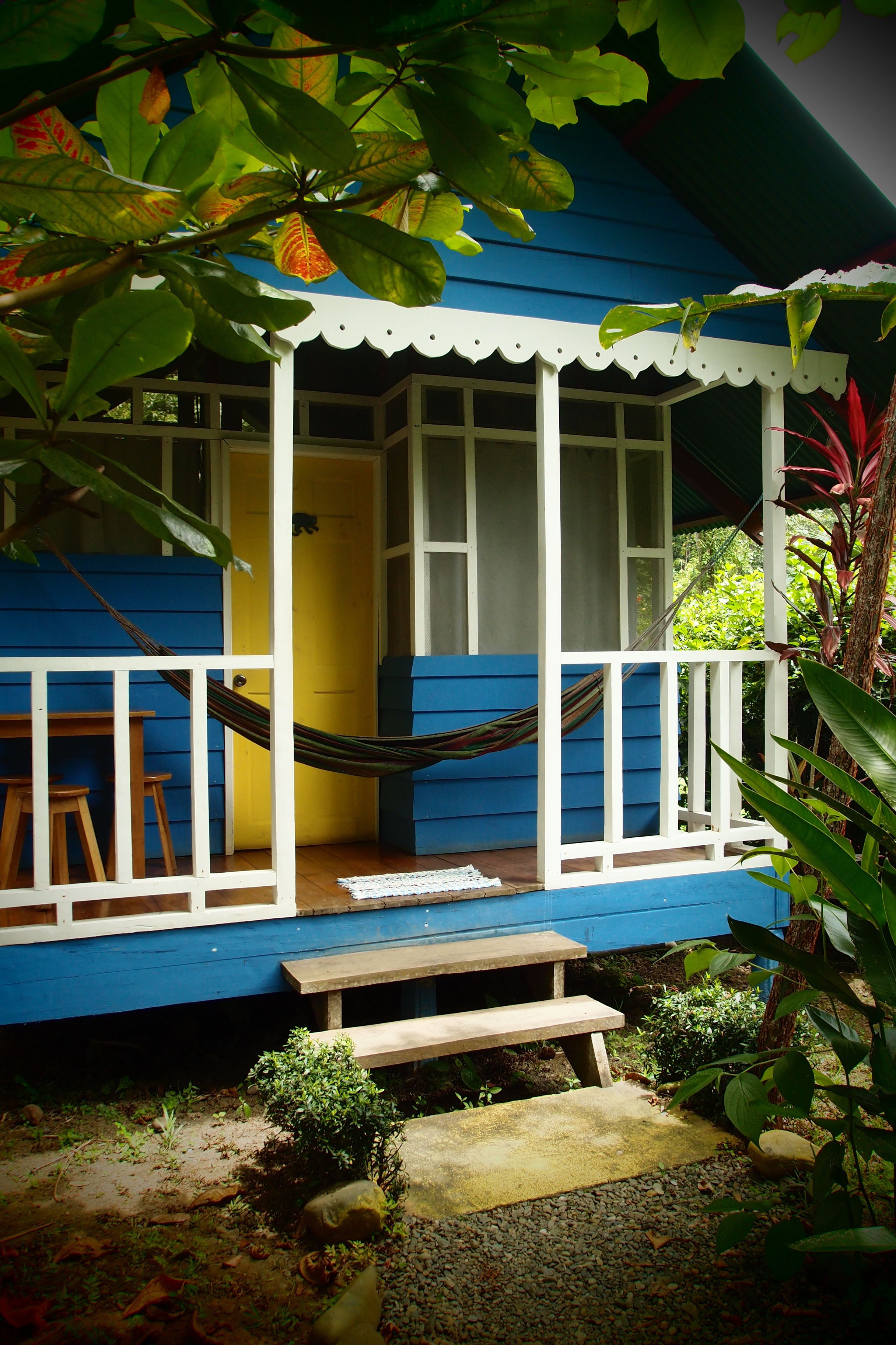 A blue house with a white porch, a hammock, and a small bench.