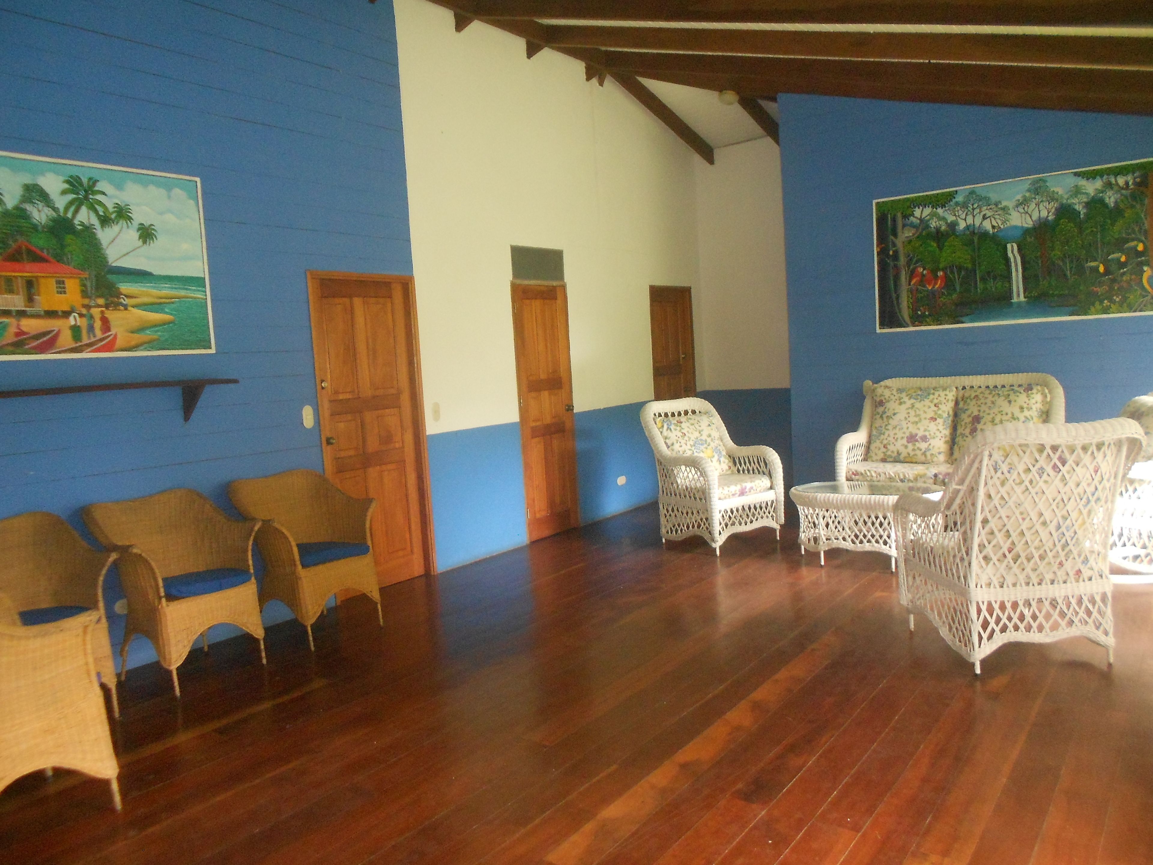 A room with wooden flooring, wicker furniture, and two doors.