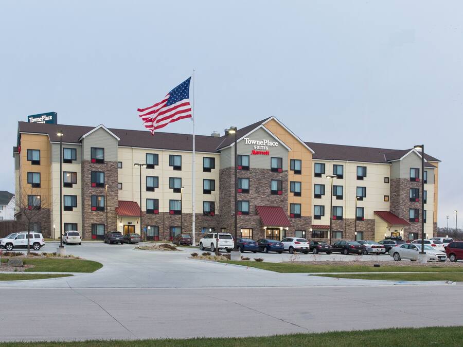 A TownePlace Suites hotel with a flagpole, multiple parking spaces, and a well-maintained lawn.