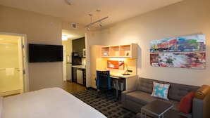 Een hotelkamer met een bed, een slaapbank, een bureau met stoel, een kitchenette en een aan de muur bevestigde televisie.