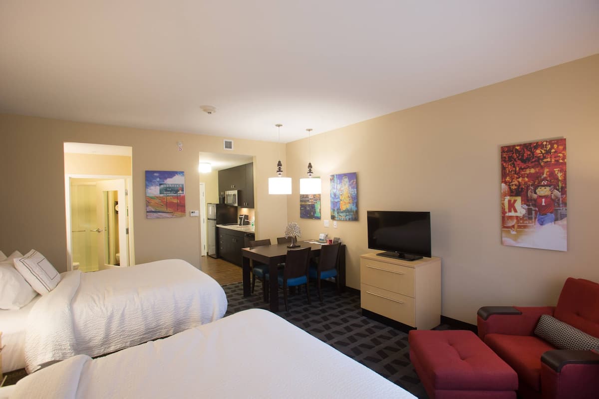 Une chambre d’hôtel avec deux lits, un bureau avec un ordinateur, une télévision et un canapé rouge.
