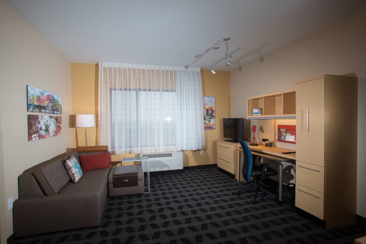 Une chambre d’hôtel de taille réduite, comprenant un canapé, un bureau avec une chaise, une télévision et une armoire.