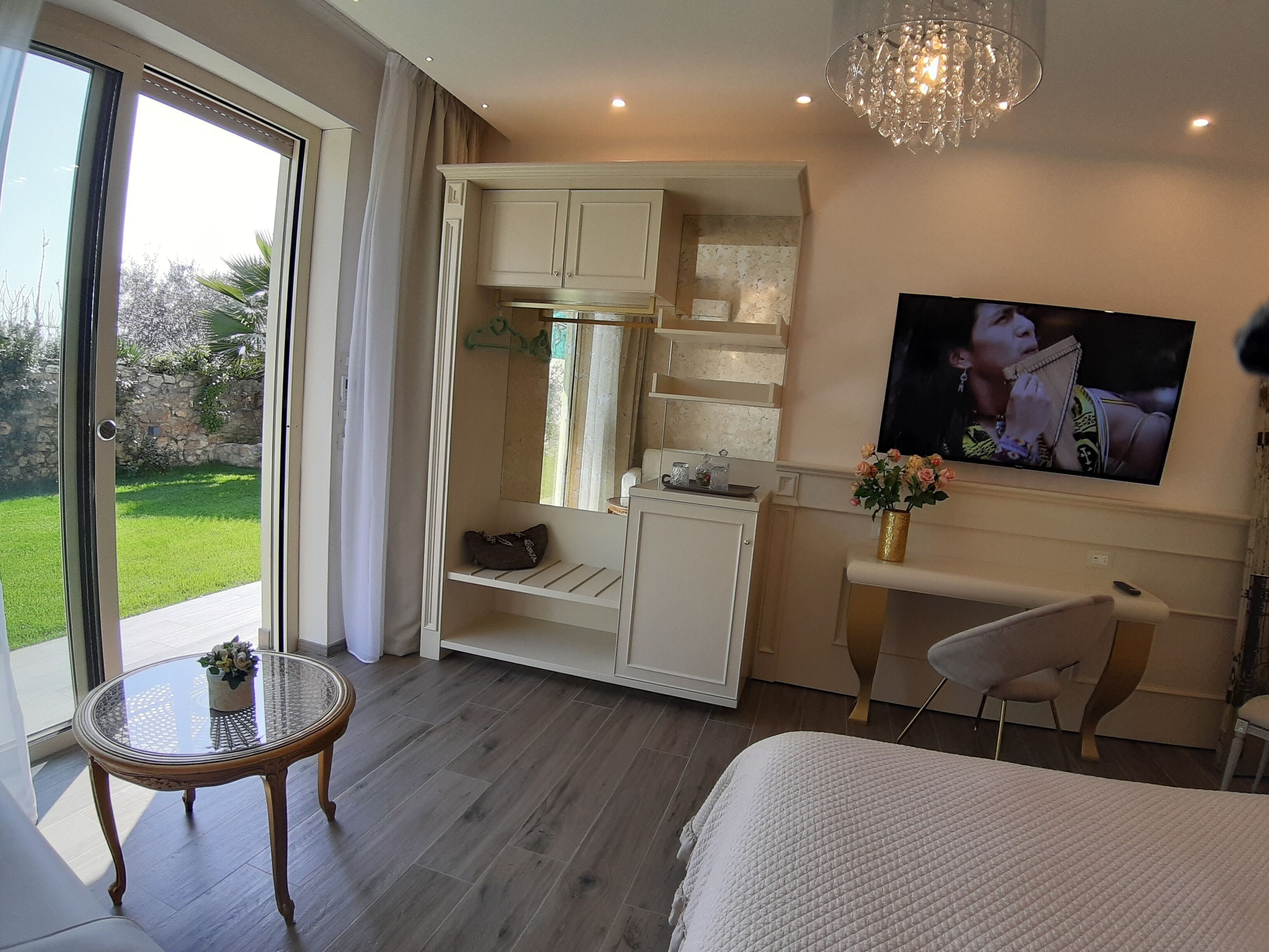 Una camera da letto moderna con una porta vetrata che dà su un balcone, una TV a parete e un tavolino con un vaso di fiori.
