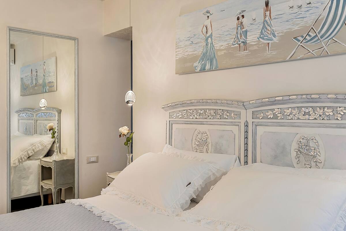 Ein Schlafzimmer mit einem großen Bett, einem Schminktisch mit Spiegel und einem Bild einer Strandlandschaft.