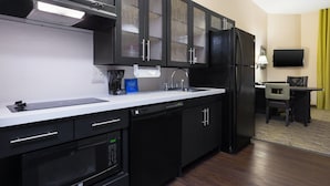 A modern kitchen with black appliances, a dishwasher, and a coffee maker. There is a dining area with a table and chairs. - Candlewood Suites Grove City - Outlet Center by IHG (Mercer)