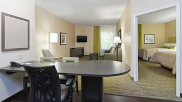 Une chambre d’hôtel équipée d’un bureau, de chaises, d’un lit, d’une télévision et d’une fenêtre avec des rideaux.