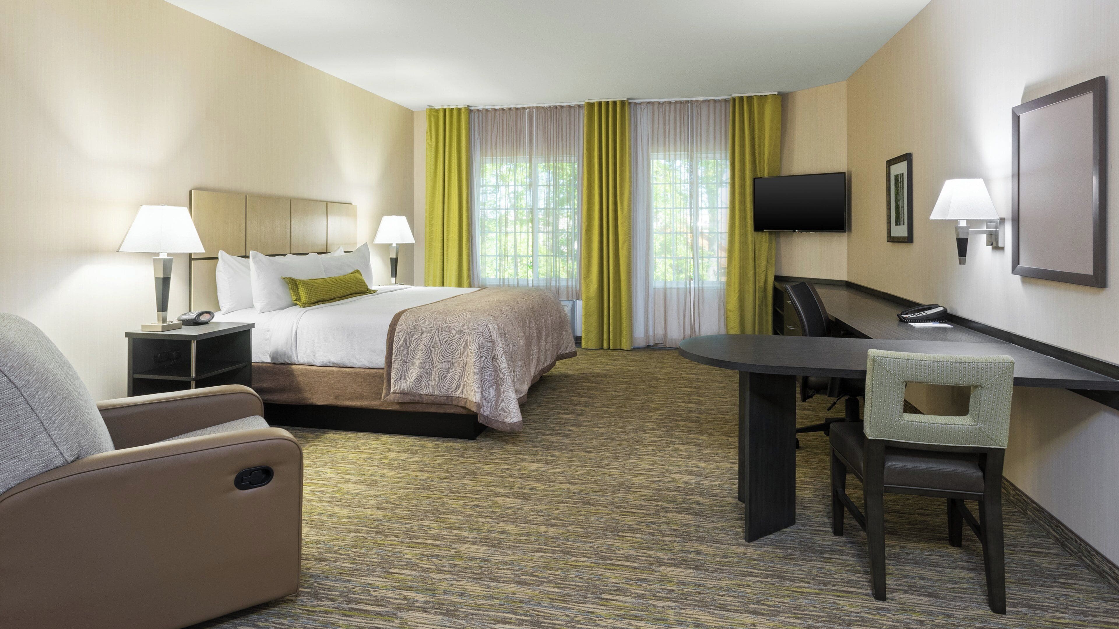 A hotel room with a bed, bedside tables, a desk with a chair, a television, and a window with curtains.