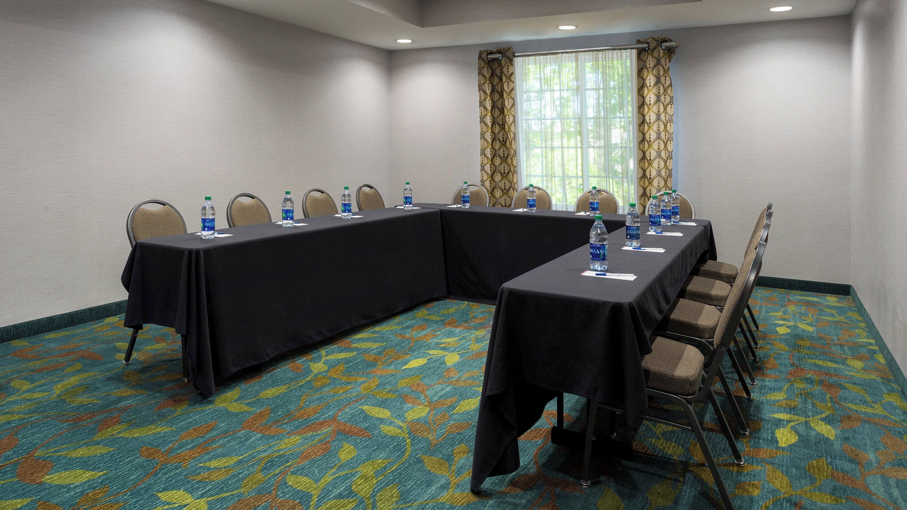 A conference room with a long table, chairs, water bottles, and a patterned carpet.