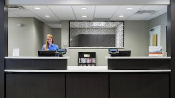 A reception desk with two computer monitors, a security camera, and a bookshelf with books.