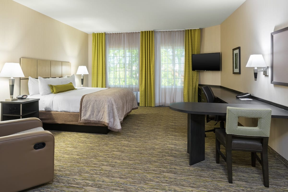 A hotel room with a bed, a desk with a chair, a TV, and a window with curtains.