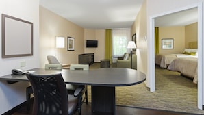 A hotel room with a desk, two chairs, a television, a bed, and a bathroom. - Candlewood Suites Grove City - Outlet Center by IHG (Mercer)