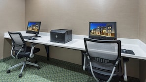 Habitación de hotel con dos escritorios, cada uno con monitor, teclado y ratón. Hay dos sillas de oficina e una impresora entre los escritorios.