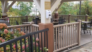 Un patio al aire libre con mesas y sillas, un cartel que indica que los utensilios de barbacoa están disponibles en la recepción y un portón de seguridad.