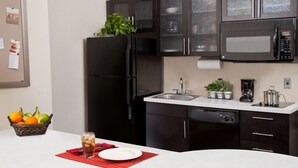 Una cocina moderna con gabinetes oscuros, un refrigerador negro, un microondas y un lavamanos. Hay una cesta de frutas y un vaso de té helado en la encimera.