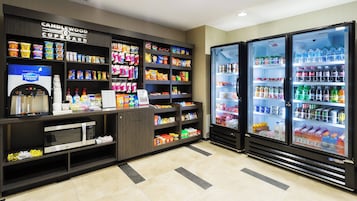 Estación de bebidas y aperitivos de autoservicio con varias opciones, que incluye un dispensador de agua, microondas y vitrinas refrigeradas.
