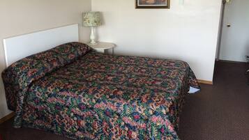 A neatly made bed with a patterned bedspread, a small bedside table with a lamp, and a painting on the wall.