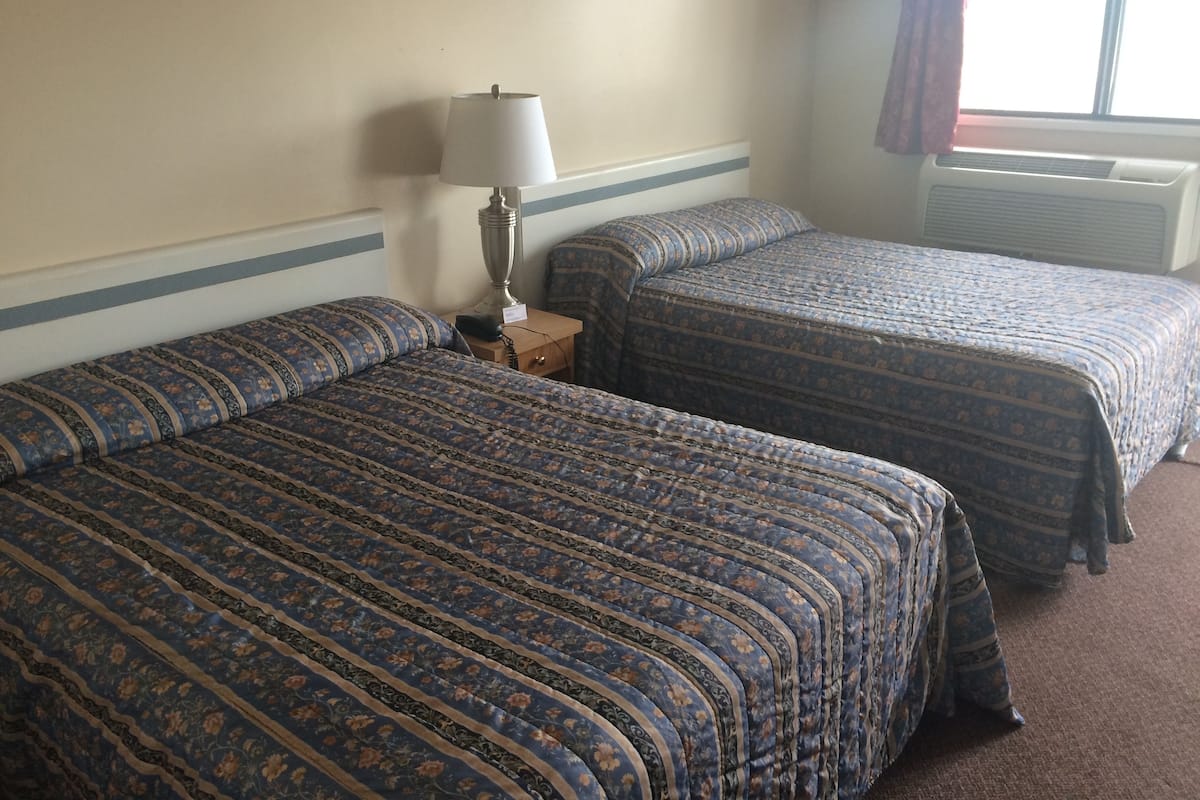 A hotel room with two beds, a nightstand with a lamp, and a window with curtains.