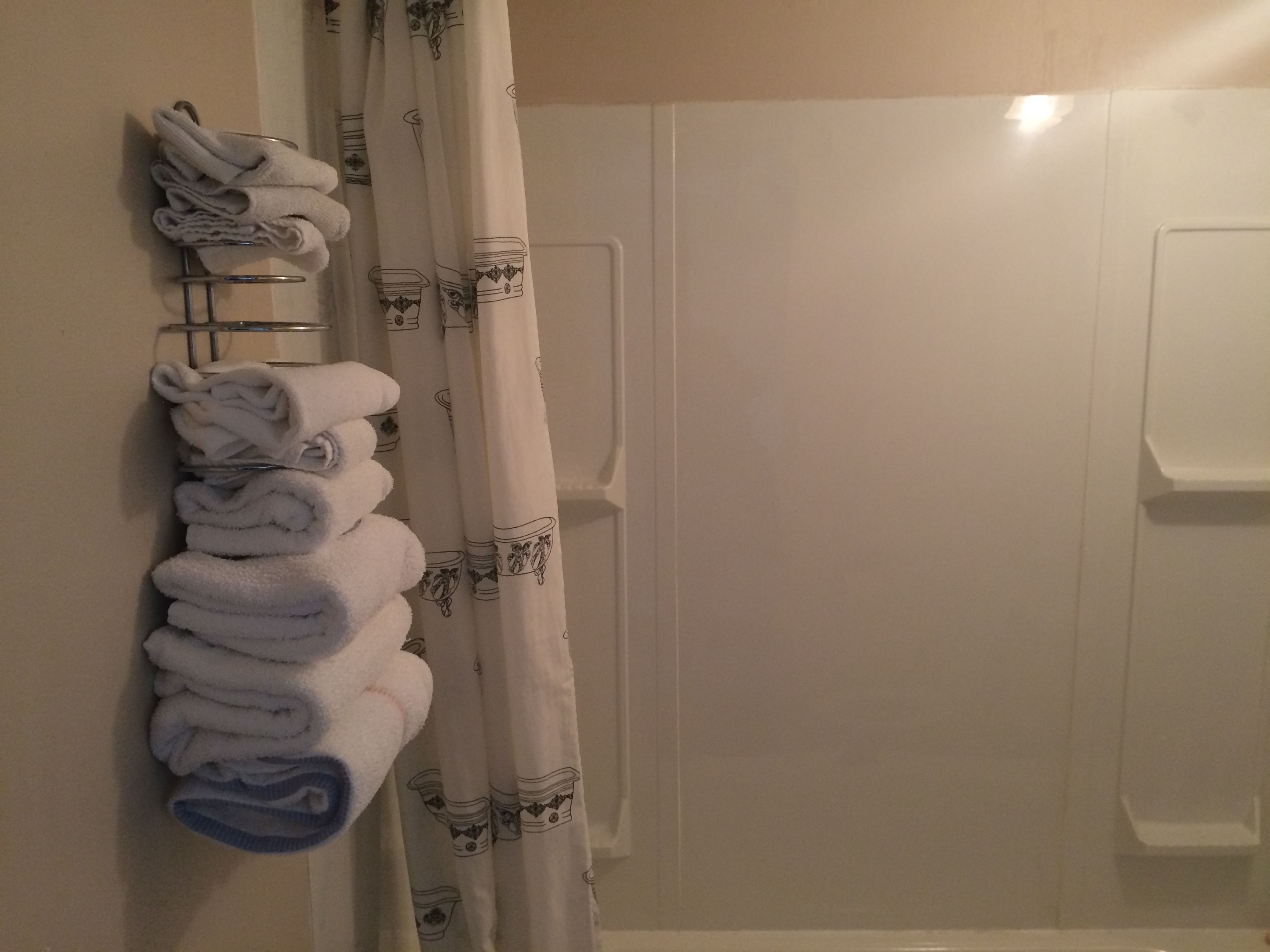 Ein Badezimmer mit einem Handtuchhalter, der ordentlich gefaltete Handtücher trägt, einem Duschvorhang mit Tassendruck und einer weißen Badewanne.