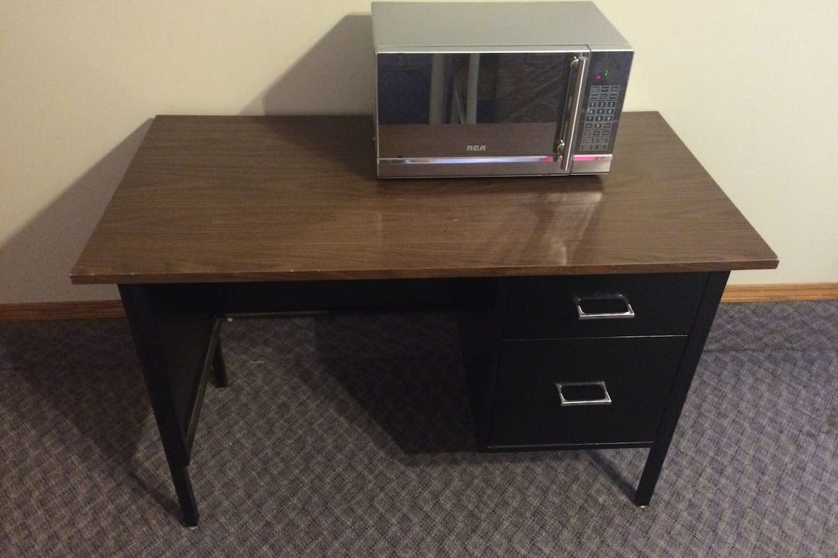 A microwave on a wooden table with two drawers.
