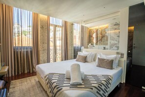 A modern hotel room with a large bed, a bathroom with a glass shower, and a view of the city. - CHARM GH by YoursPorto (Vila Nova de Gaia)