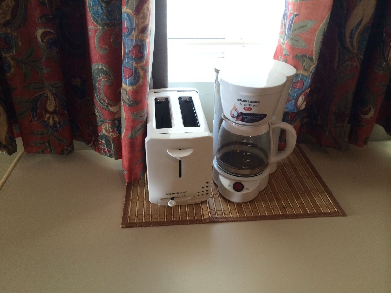 A kitchen area with a toaster and a coffee maker on a mat.