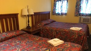 Habitación de hotel con dos camas, una mesita de noche con lámparas y una ventana con cortinas estampadas.