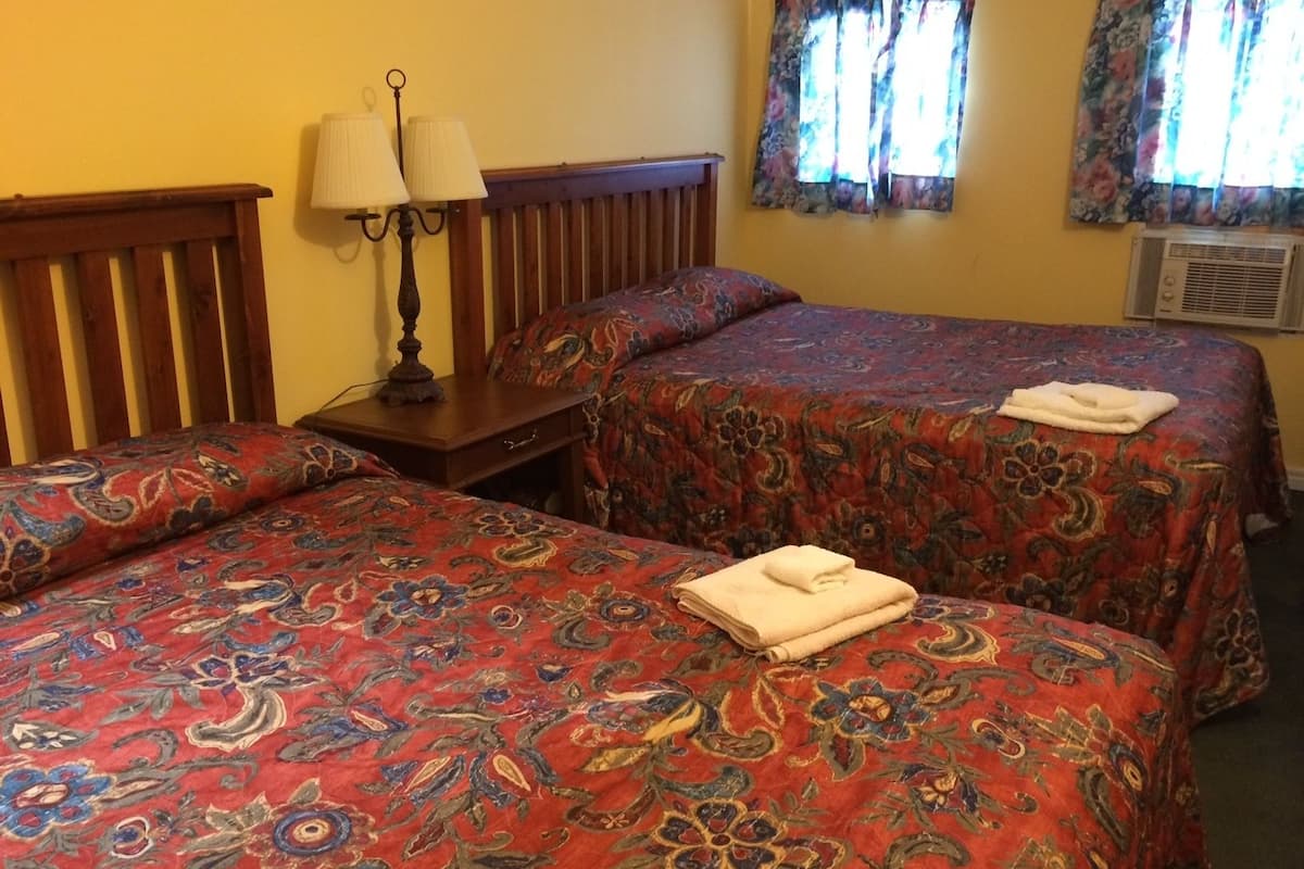 Une chambre d’hôtel avec deux lits, une table de chevet avec des lampes et une fenêtre agrémentée de rideaux à motifs floraux.