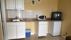 Una cocina compacta con gabinetes blancos, un microondas, un refrigerador pequeño y un televisor sobre la encimera.