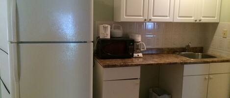 A compact kitchen with white cabinets, a refrigerator, a microwave, and a coffee maker.