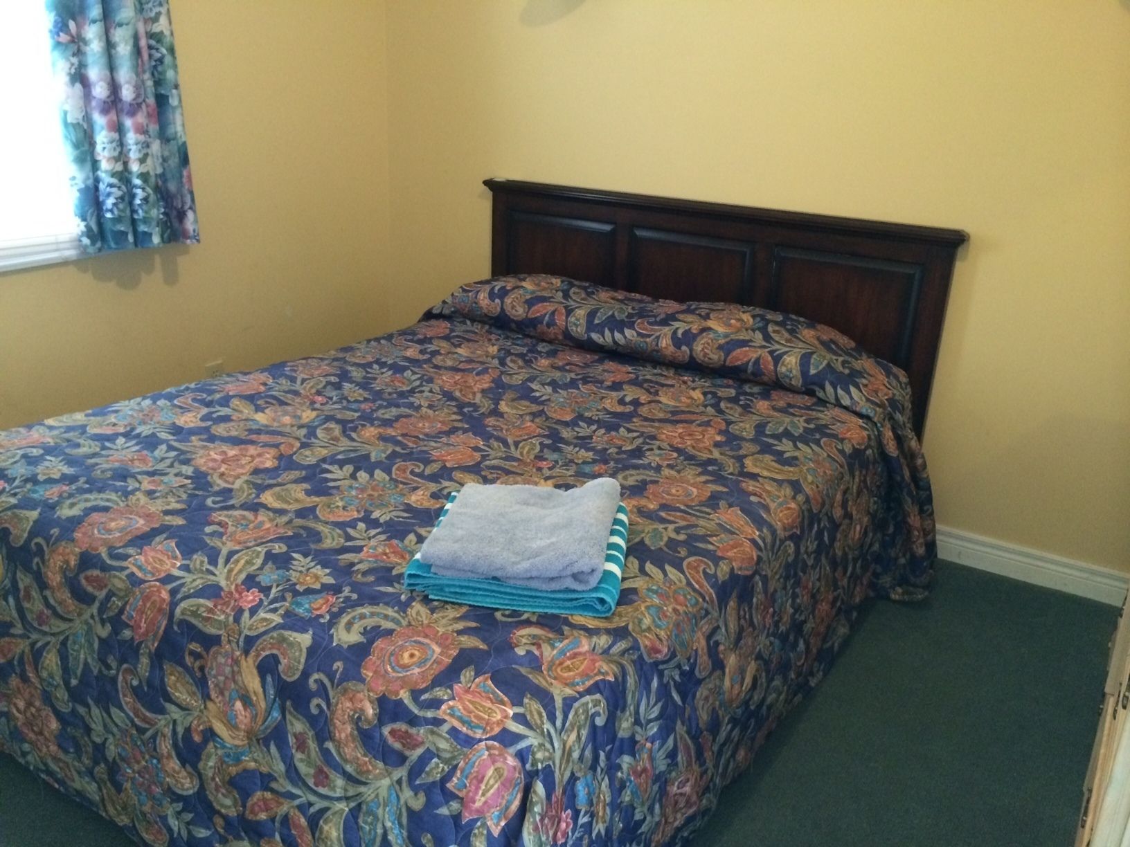 A bed with a floral-patterned bedspread and a neatly folded towel on top.