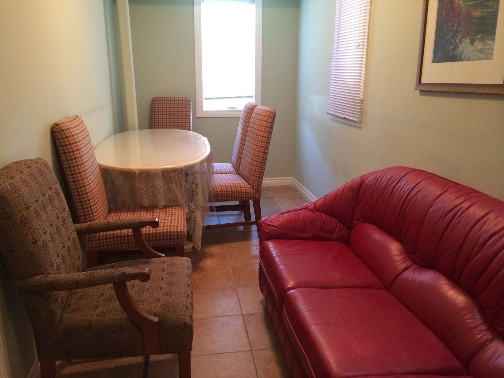 A living room with a red leather couch, a round table with a lace tablecloth, and two plaid chairs.