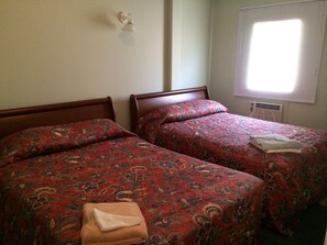 Een kamer met twee bedden, elk voorzien van een bloemenprintdeken, een wandlamp en een raam met jaloezieën.