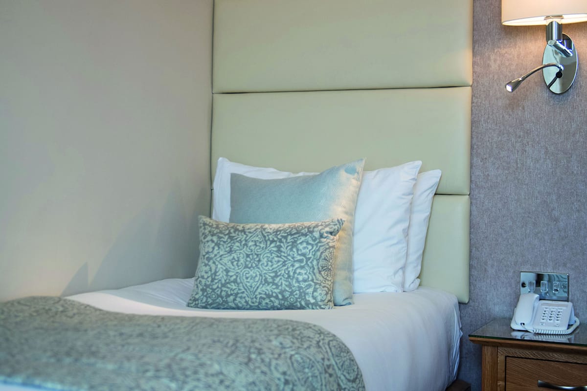 Ein Hotelzimmer mit Bett, Nachttisch mit Telefon und einer Wandlampe.