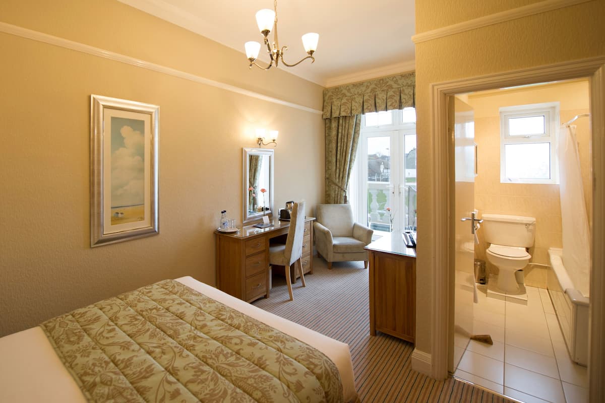 Ein Hotelzimmer mit einem Bett, einem Schreibtisch mit Stuhl, einem Spiegel, einer Chandelier und einem Badezimmer mit Toilette und Waschbecken.