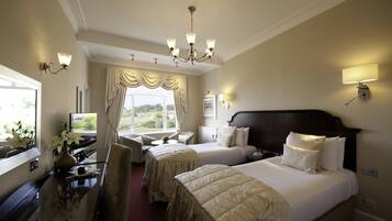 A hotel room with two beds, a sitting area with a chair and table, a view of the outdoors through a window, and a chandelier.