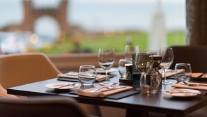 A dining table set with glasses, plates, and cutlery, overlooking a scenic view with a distant structure. - The Belmont Hotel - Adults Only (Sidmouth)