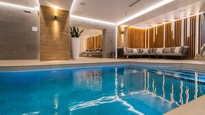A modern indoor swimming pool with a clear blue water, a lounge area with a sofa and chairs, and a wooden wall with vertical slats. - The Belmont Hotel - Adults Only (Sidmouth)